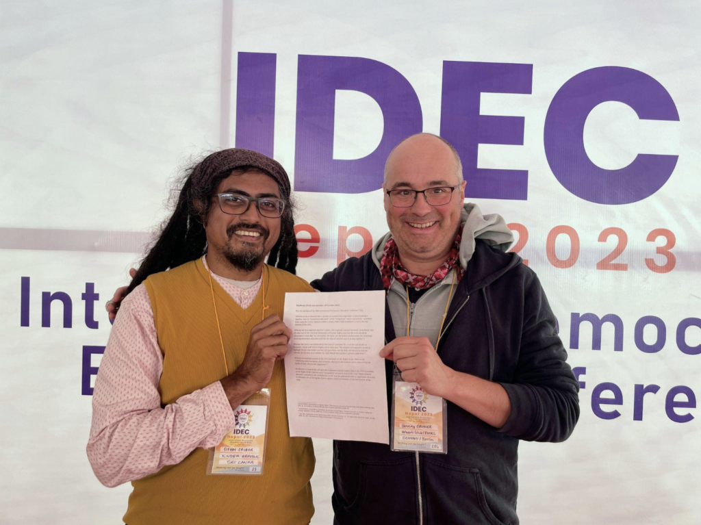 Photo showing Sifaan Zavahir of Sri Lanka and Henning Graner of Germany present the IDEC Resolution 2023 adopted by the International Democratic Education Conference in October 2023 in Nepal